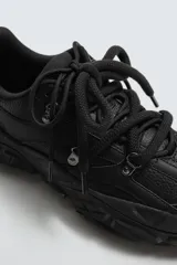 Zapatilla deportiva de estilo running con diseño robusto y suela de volumen irregular. Presenta una parte superior confeccionada en una combinación de piezas texturizadas y detalle de doble cordonera.