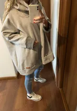 Canguro gris claro con cuello alto, mangas largas con puños en gris oscuro, bolsillo tipo canguro y corte holgado.