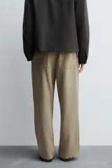 Pantalón negro de corte relajado con cintura elástica ajustable y pliegues en la parte delantera. Presenta bolsillos laterales y bolsillos traseros de parche.