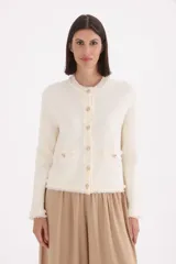 Saco de punto estilo tweed en color natural, con cuello redondo, cierre frontal de botones dorados y detalles de flecos en los bordes, puños y bolsillos frontales.