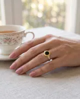 Anillo de plata 925 con diseño redondo, piedra ónix central y detalle de lámina de oro de 18k con guarda griega alrededor.