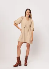 Vestido corto color beige, de corte oversize, con escote en V y mangas globo. Incluye cinturón marrón con hebilla dorada.