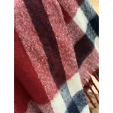 Bufanda rectangular de tejido grueso con diseño de cuadros en tonos azul, naranja, gris y beige, terminada con flecos en los extremos.