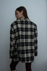 Blazer de corte oversize con estampado de cuadros en tonos negro y beige. Presenta solapas clásicas, cierre frontal con botones y bolsillos laterales con solapa.