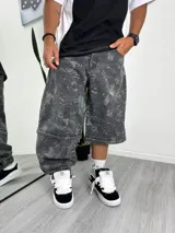 Pantalón de mezclilla gris oscuro con efecto lavado y estampado sutil de hojas o ramas en tono más claro. Diseño de corte muy ancho (baggy) que se puede convertir en short a la altura de la rodilla mediante cierres.