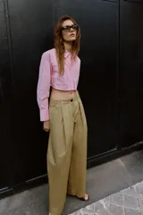 Camisa corta rosa con rayas verticales finas, cuello solapa, manga larga y bolsillos delanteros de plastrón. Cierre frontal con botones ocultos.