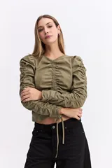 Blusa de manga larga color marrón chocolate, con diseño fruncido central ajustable mediante cordones y mangas con detalle de frunces laterales que aportan volumen.
