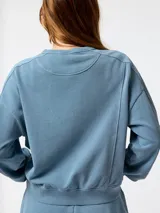 Buzo oversize color celeste de cuello redondo, con mangas largas y puños de rib elástico. Presenta un pequeño logo bordado en el pecho.