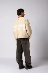 Buzo oversize de corte boxy, confeccionado en algodón rústico de alto gramaje en color beige. Presenta cuello redondo con borde crudo, mangas largas y una estampa frontal con el texto VCP delimitado por líneas horizontales blancas.