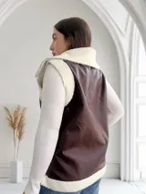 Chaleco marrón de ecocuero con interior de corderito blanco, cierre frontal con cremallera y bolsillos laterales.