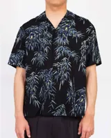 Camisa de manga corta negra con estampado de bambú en tonos azules y amarillos, cuello cuban y cierre frontal de botones.