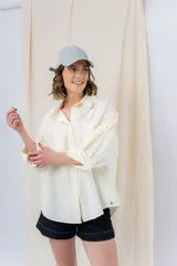 Camisa verde pastel de algodón, corte oversize, con cuello camisero, cierre con botones, mangas largas con puños con volados de encaje blanco, dos bolsillos frontales con solapa y ruedo irregular. 