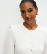 Cardigan de punto color blanco, de corte regular y ajuste al cuerpo. Presenta cuello redondo, mangas largas, cierre frontal con botones delicados y hombreras estructuradas que aportan volumen a la silueta.