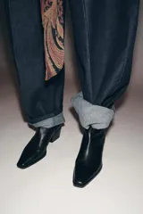 Botín de cuero negro estilo cowboy, con tacón medio ancho y punta fina. Cuenta con cierre mediante cremallera lateral.