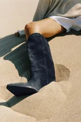 Bota alta de estilo cowboy confeccionada en serraje de color azul marino, con tacón medio en bloque y puntera perfilada. Presenta costuras decorativas en el cuerpo y diseño de calce fácil.