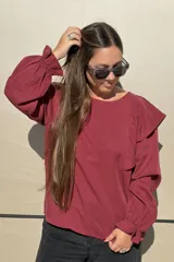 Blusa de algodón color bordó, con diseño de volados en los hombros, mangas largas con puños elásticos y corte holgado.