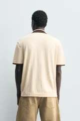 Camisa de punto de algodón con corte relajado, cuello solapa y manga corta. Presenta un diseño bicolor en tonos beige y marrón, con cierre frontal de botones.