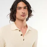Remera tipo polo de manga corta confeccionada en tejido de punto con textura acanalada, color beige, con cuello camisero y cartera de tres botones carey.