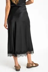 Falda midi negra de acabado satinado, corte al bies, con detalle de encaje en el ruedo.