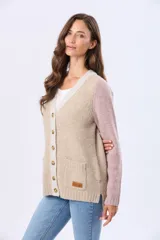 Saco tipo cárdigan de tejido grueso con diseño en bloques de color, combinando tonos beige y rosado. Presenta cuello en V, cierre frontal con botones y dos bolsillos delanteros.