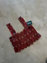 Top tipo corset o bustier de color bordó con textura de piel de cocodrilo. Presenta pliegues horizontales y está adornado con múltiples ojales metálicos dorados a lo largo de todo el cuerpo y tirantes.