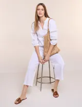 Pantalón crop de lino y algodón color blanco, con calce holgado, pierna ancha de corte recto y cintura elástica. Presenta bolsillos laterales y detalle de puntilla aplicada en el frente.