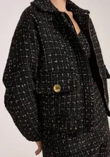 Chaqueta de tweed color negro con hilos metalizados, diseño estructurado, cuello solapa y cierre frontal con cremallera.
