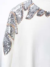 Buzo color crudo de mangas largas con apliques de lentejuelas plateadas y doradas en los hombros.