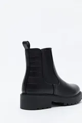 Bota tipo chelsea de caña baja con suela dentada robusta. Presenta un diseño combinado con paneles laterales elásticos, acabado liso en el frente y detalle texturizado en relieve en la parte posterior, incluyendo un tirador trasero para facilitar el calce.