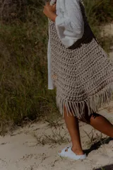 Bolso de mano grande tejido a crochet con técnica de trapillo reciclado, color beige visón. Presenta un diseño de punto grueso y flecos largos en el borde inferior.