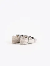Zapatillas de cuero vacuno en color beige, con recortes de gamuza en la puntera y talón, doble cordón en tonos gris y marrón, hebilla lateral y dije colgante en la cordonera. Suela plana de goma.
