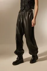 Babucha de cuero sintético color negro, con cintura elástica y puños ajustados en los tobillos. Presenta un diseño holgado y moderno con costuras horizontales en las piernas.