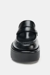 Mocasín destalonado de estilo mule, color negro, con diseño de antifaz y suela de plataforma dentada tipo chunky.