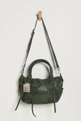 Cartera de cuero verde militar con acabado gastado, cuerpo blando, asas de mano, bolsillos frontales con cierre y tiras colgantes.