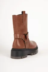 Bota estilo biker de cuero sintético color negro, con suela tipo plataforma dentada. Presenta una tira decorativa con argolla metálica y apliques de tachas en el tobillo.