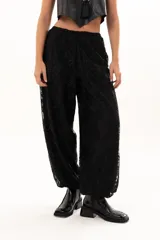 Pantalón de encaje negro con diseño floral, corte holgado y cintura elástica con cordón ajustable. Cuenta con bolsillos laterales.