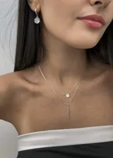 Collar plateado de doble cadena, con dije circular con circonitas y dije de barra vertical.