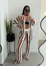 Conjunto de dos piezas tejido a crochet con diseño de rayas verticales en color marrón y blanco. Incluye una camisa de manga corta con cuello y botones frontales, y un pantalón de corte recto y tiro alto.