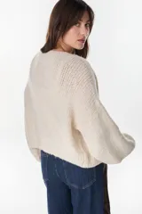 Cardigan crop de punto color crudo, con frente abierto sin botones y mangas largas abullonadas.