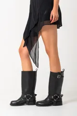 Borcegos de caña alta (30 cm) color negro, confeccionados en ecocuero, con suela gruesa y bajo relieve. Presentan una correa con hebilla metálica plateada alrededor del tobillo y una correa ajustable con hebilla en la caña superior.