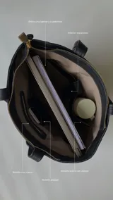 Cartera tipo tote de cuero graneado negro, con diseño clásico y textura uniforme. Cuenta con doble asa de hombro, bolsillo frontal con cierre magnético, bolsillo trasero con cierre metálico y compartimento principal con cierre. El interior está forrado y dispone de múltiples bolsillos organizadores.