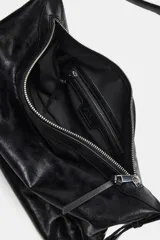 Bolso tipo saca color negro, de diseño flexible y acabado con efecto gastado. Cuenta con un asa ajustable para el hombro, detalles de hebillas y herrajes metálicos laterales, además de un cierre superior de cremallera metálica.