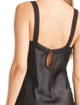 Vestido lencero negro de satén con acabado brillante, corte al bies, escote en V pronunciado con ribete de encaje, aplique horizontal de encaje calado debajo del busto, breteles anchos de encaje elástico y espalda con abertura gota. La falda termina a media pierna.