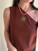 Collar corto con cadena de eslabones dorados y cuentas de nácar y mostacillas en tonos rosado, naranja y coral. Incluye un dije grande en forma de sol estilizado en metal dorado.