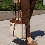 Bolso tipo tote de cuero color marrón con detalles en negro. Tiene doble asa de hombro y correa extraíble regulable. Incluye cierre principal y bolsillo interior.