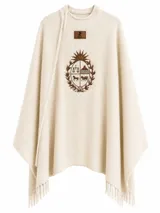 Ruana de lana merino color beige con diseño de tejido en espiga. Presenta un bordado central del Escudo Nacional en color marrón y terminaciones con flecos en el ruedo.
