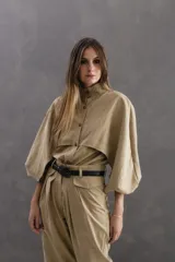 Camisa de seda peletizada color beige, con diseño de sobrecapa integrada, cuello mao y mangas abullonadas. Presenta cierre frontal con botones al tono.