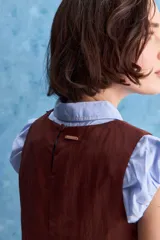 Top blanco sin mangas, con cuello redondo, diseño cruzado en el frente y cierre con botones en el hombro.