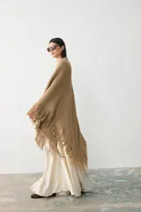 Ruana tejida en lana merino extrafina con lino y viscosa, de diseño triangular con textura en relieve y flecos en los bordes. Pieza versátil de calce holgado y envolvente.