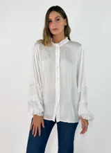 Camisa de satén color blanco, con cuello alto estilo mao con volados, cierre frontal de botones y mangas largas con detalles de volados escalonados en los puños.
